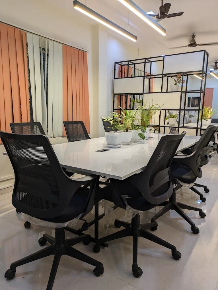 Front view of the meeting table at Full Stack World — black mesh chairs, plants, feature bookshelf in the background